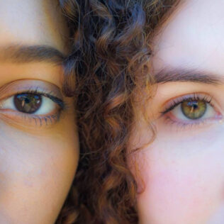 Close up faces of a pale skinned and darker skinned female looking directly at camera