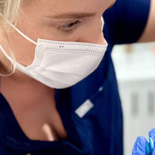 Dr Ciara Daly in SkinBox uniform wearing face mask injecting patient