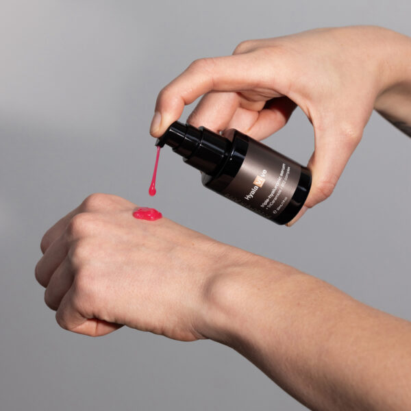 hyalavive serum being pumped out onto back of hand to show pink colour of product